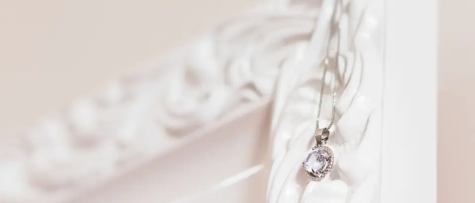 A silver pendant on a fine chain hanging from a white carved frame