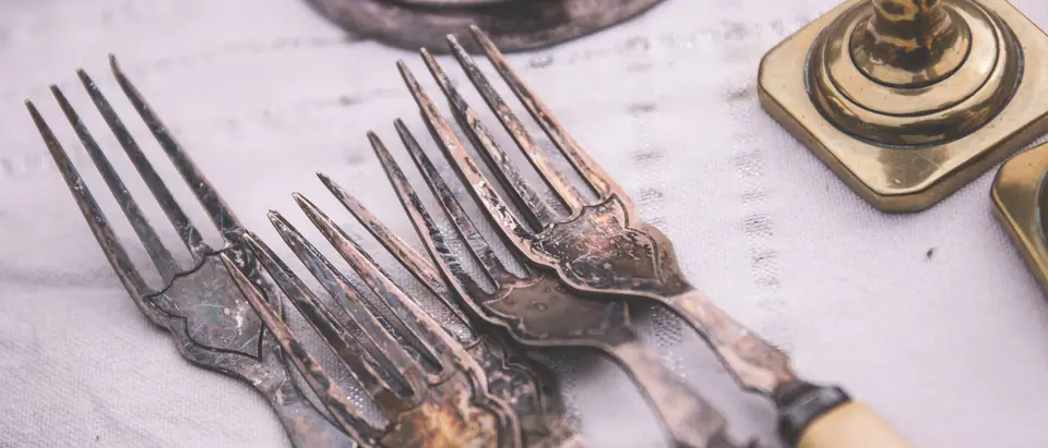 Vintage silver forks with bone handles beside a brass candlestick on a white cloth