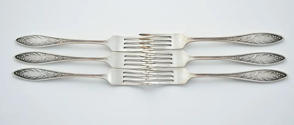 Three engraved silver forks laid head to tail on a pale grey ground