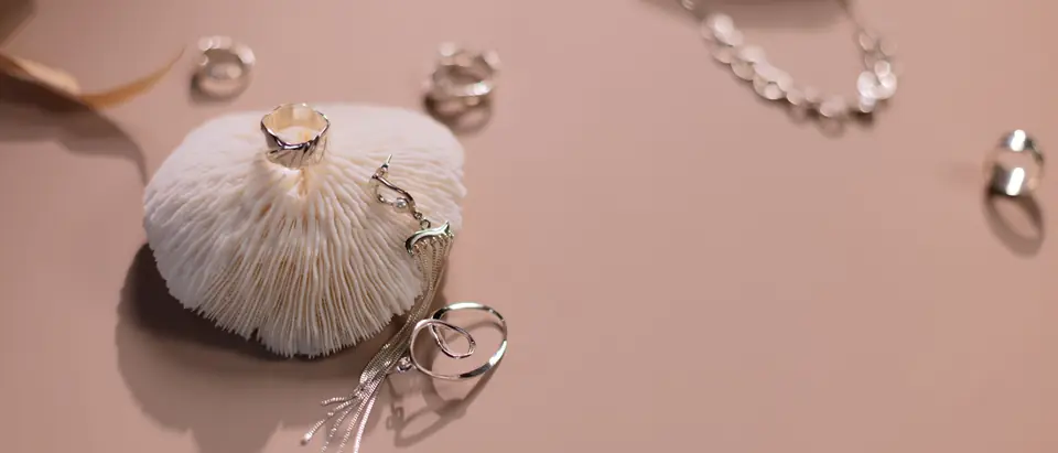 Silver rings and a fine silver chain laid out on a soft pink ground