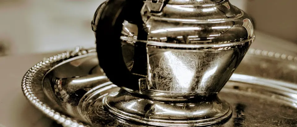 A polished silver teapot with a black handle on a beaded silver tray