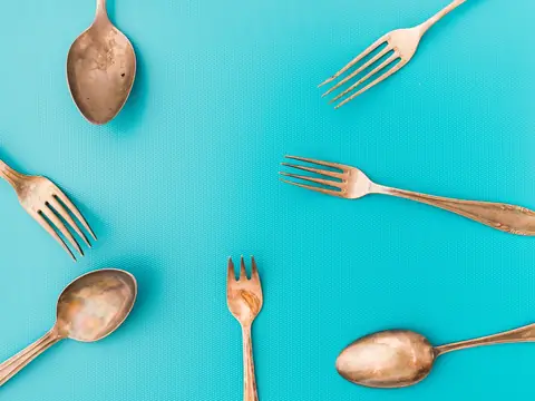 Old plated forks and spoons worn through to a copper-coloured base metal, on a turquoise ground