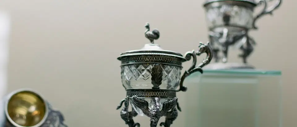 Two antique silver sugar bowls with cut-glass liners on a glass shelf