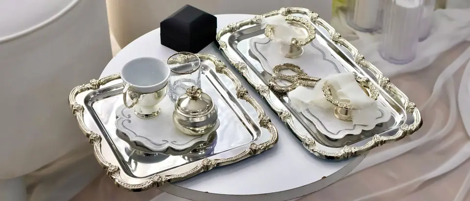 Two ornate silver trays holding a small tea service on a white table