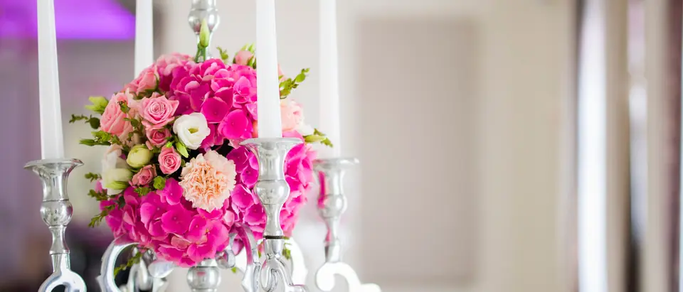 A silver candelabra with white candles and a bouquet of pink roses and hydrangeas