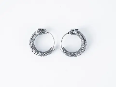A pair of silver hoop earrings shaped as dragons on a white ground