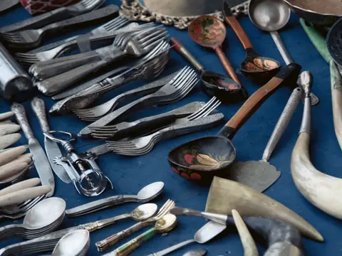 Old spoons, forks, knives and horn-handled serving pieces spread across a blue cloth