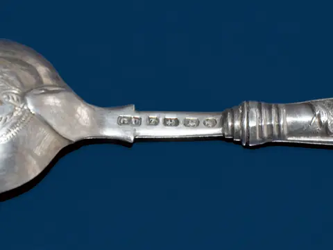 The back of an 1899 Birmingham silver spoon, the maker's GU and the lion passant for sterling struck on the stem