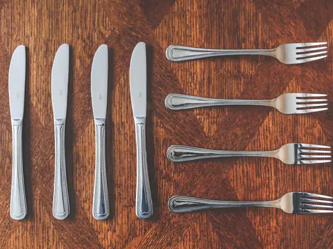 Silver knives and forks laid out in rows on a wooden table
